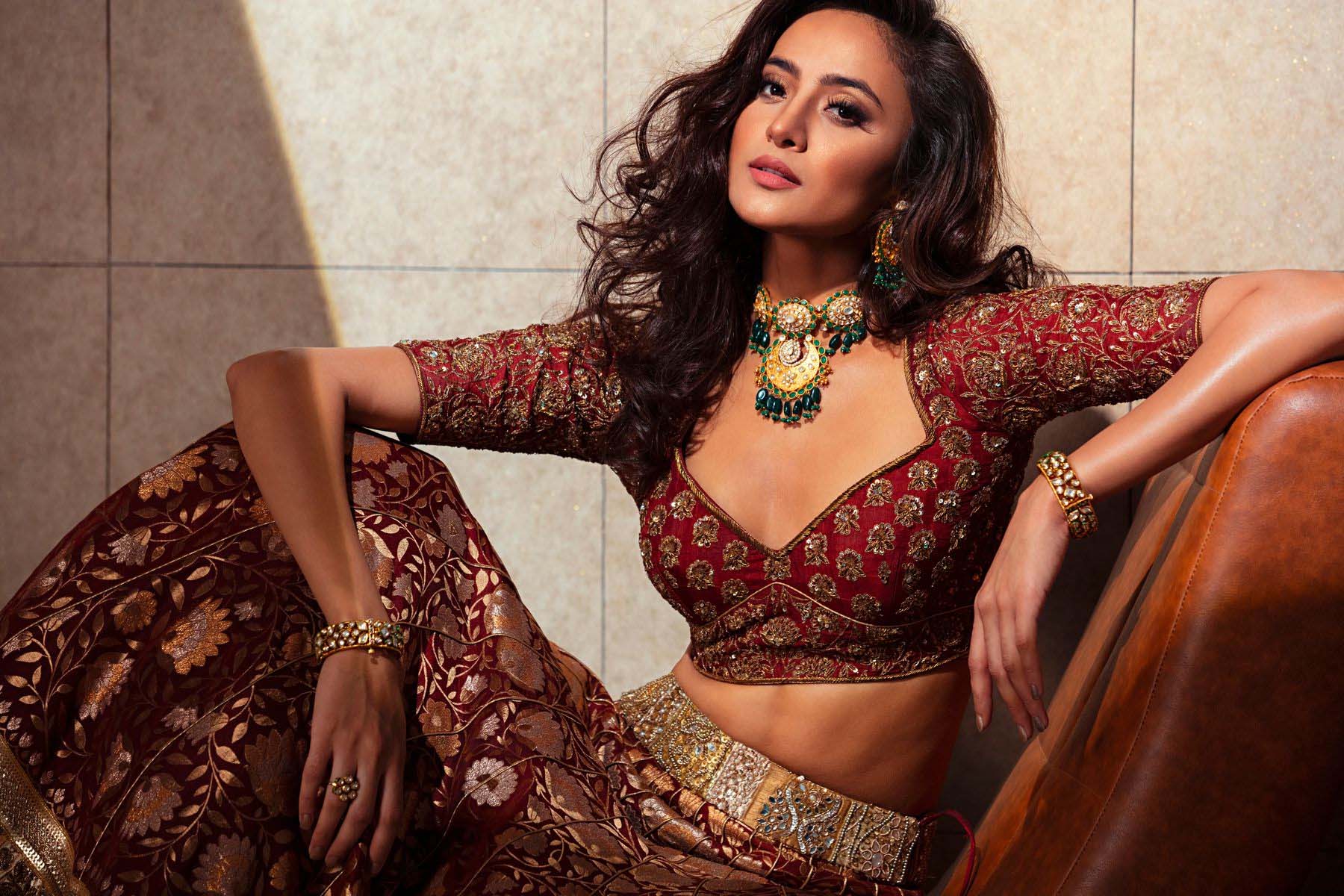 Bride in maroon embroidered lehenga with statement jewellery and bracelets, standing with soft curls and confident pose.
