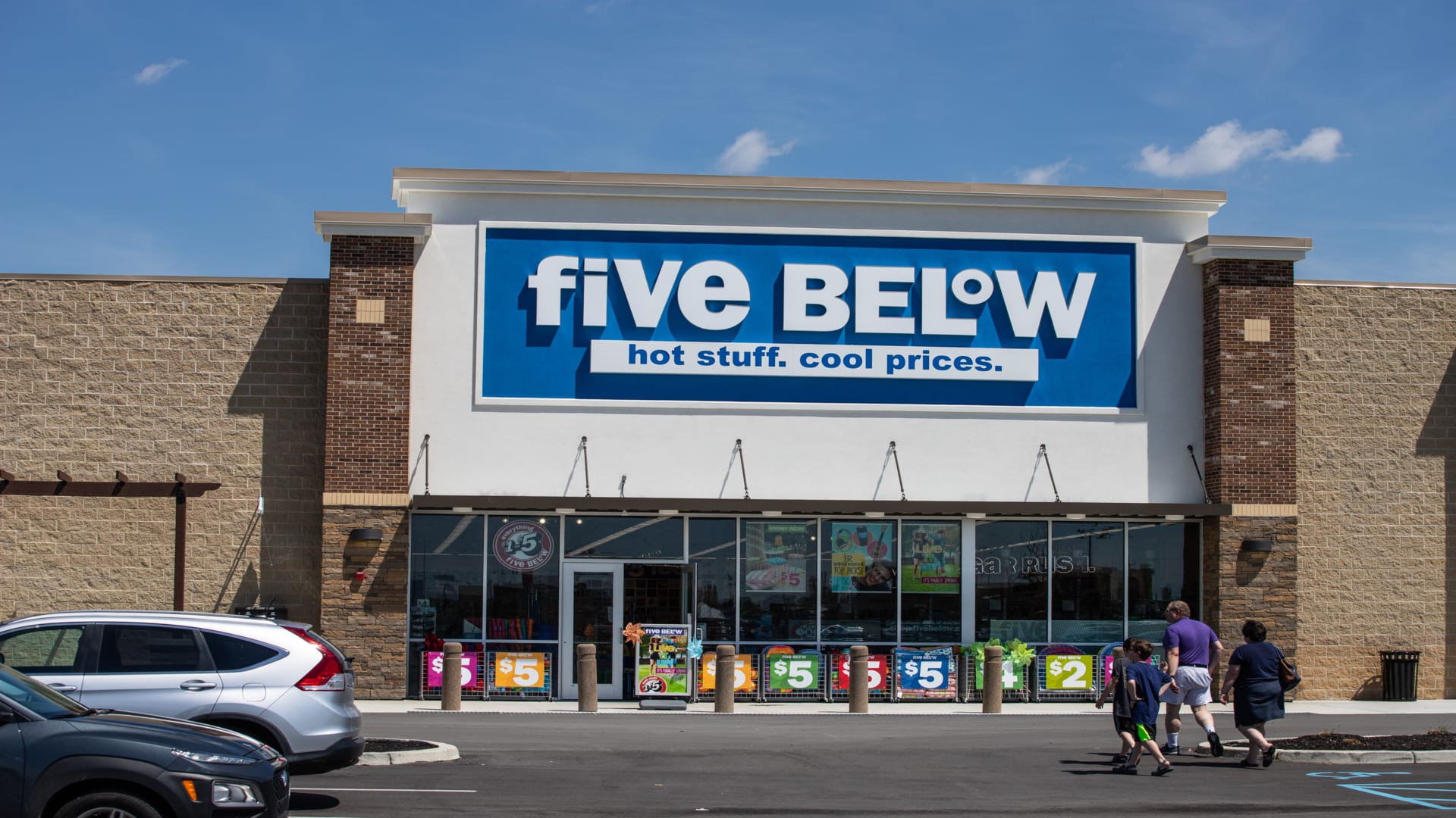 The exterior of a Five Below store is shown with a family walking toward the door.