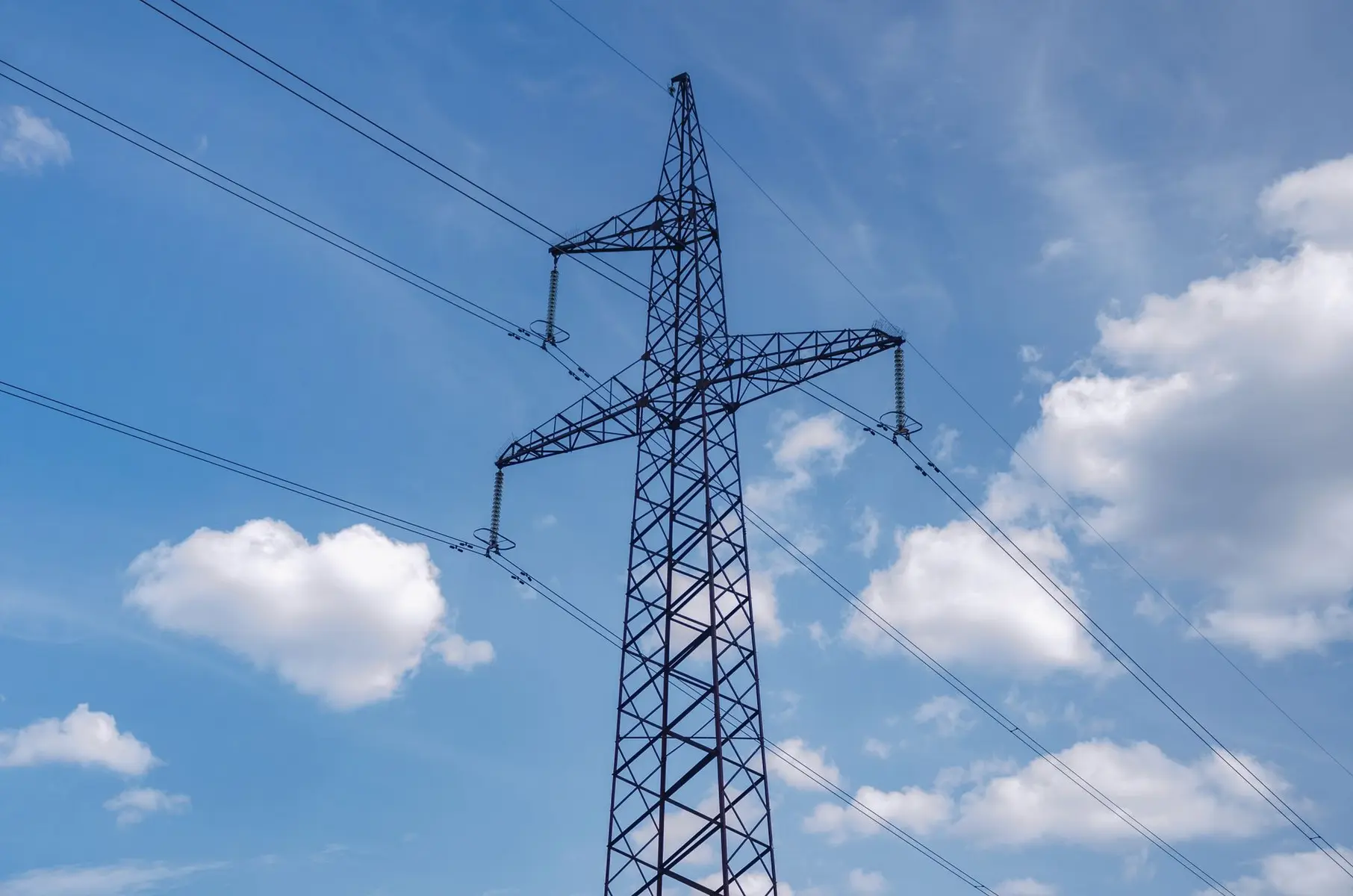 High-voltage steel lattice transmission tower supporting electrical power lines against a blue cloudy sky