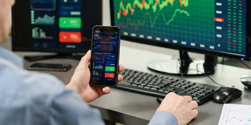 man trading using moible phone and multiple screens | best indicators for day trading