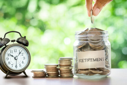 Hand putting Coins in glass jar with a label that says "retirement"